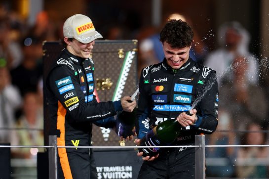 ABU DHABI, UNITED ARAB EMIRATES - DECEMBER 07: Second placed Oscar Piastri of Australia and McLaren and 2025 F1 World Drivers Champion and Third placed Lando Norris of Great Britain and McLaren celebrate on the podium with Champagne during the F1 Grand Prix of Abu Dhabi at Yas Marina Circuit on December 07, 2025 in Abu Dhabi, United Arab Emirates. (Photo by Zak Mauger/LAT Images)